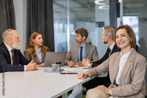 Attractive young businesswoman sitting on the table, looking at camera with colleagues on the background