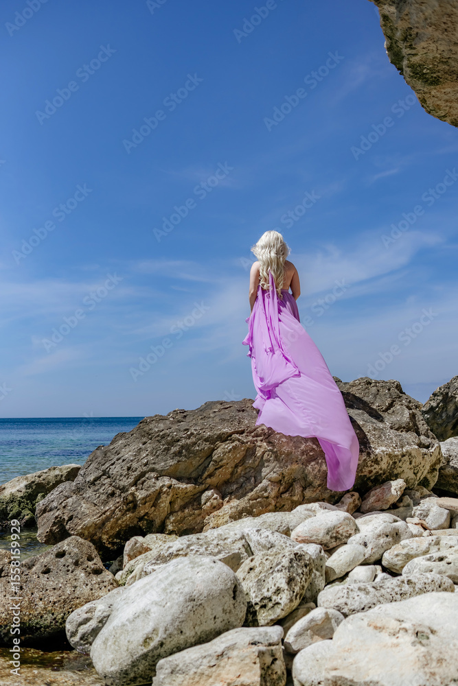Woman Rock Beach: Woman in purple dress stands on rocks at beach during sunny day for photoshoot. Woman Rock Beach: Woman in purple dress stands on rocks at beach during sunny day for photoshoot.