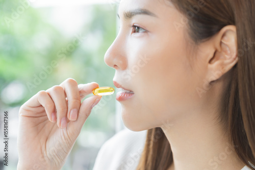 Dietary supplement, beautiful asian young woman, girl hand holding fish oil pills, drugs medical, take or eat vitamin for treatment skin, hair and nail strengthen at home. Healthcare medicine concept
