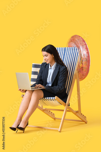 Young businesswoman using laptop in deck chair on yellow background. Summer vacation concept