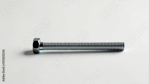 A metallic hex bolt with a threaded shaft lies on a plain, light-colored surface.