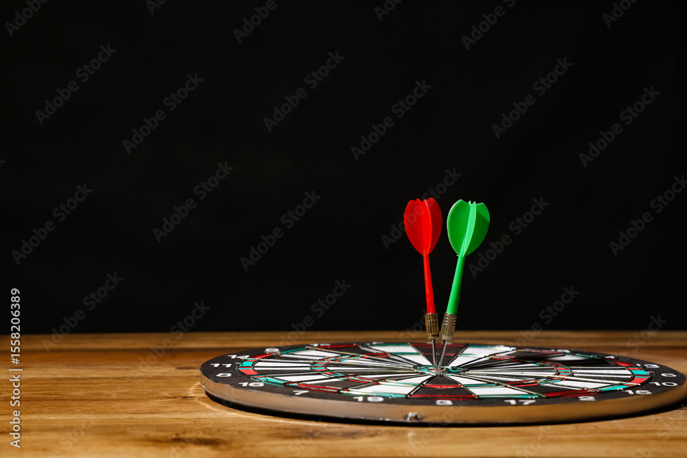 Fototapeta premium Board with darts on wooden table against dark background