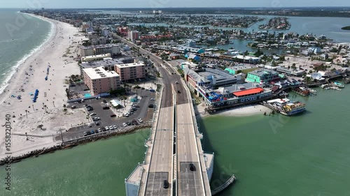 Aerial backwards shot of driving cars on John's Pass Bridge in Florida at sunny day. Wide shot. Sandy beach with relaxing people in Madeiras beach City. Coastline luxury houses and islands in back.