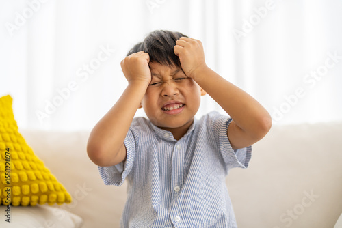 Portrait of sick depressed unhappy child boy touching on head feel suffering head ache pain flu high fever, alzheimer, cancer, stroke, parkinson, disease, cerebral haemorrage, encephalitis, dementia
