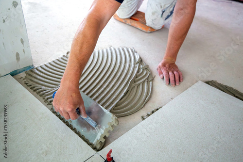 Fliesenverlegung: Fliesenleger verlegt große helle Bodenfliesen