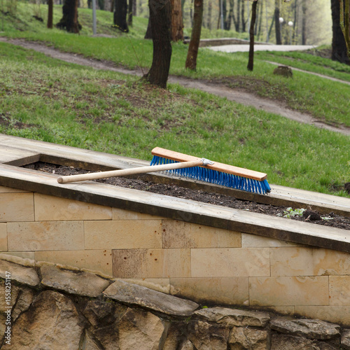 Blue brush on wooden handle lying on stone planter wall in park setting