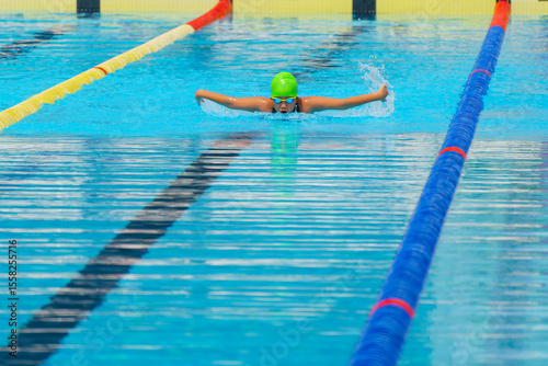 Swimmer child swims butterfly swimming style in a race swimming pool. Water sports and competition, learning to swim classes for children.