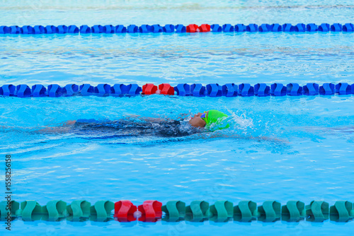 Swimmer child swims backstroke swimming style in a race swimming pool. Water sports and competition, learning to swim classes for children.