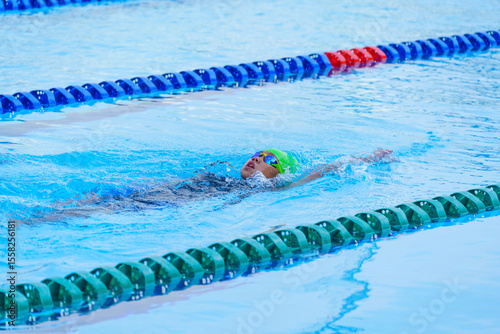Swimmer child swims backstroke swimming style in a race swimming pool. Water sports and competition, learning to swim classes for children.