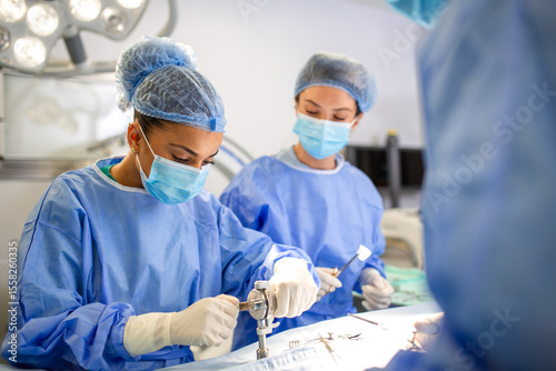Female surgeon using orthopedic surgical equipment during a medical procedure. Concentrated and precise movements under bright operation lights with other team members assisting in background. photo