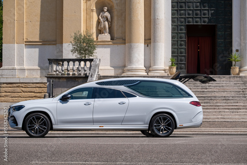 Fotografie White funeral car with open trunk near Italian church entrance