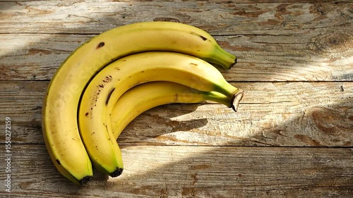 Three ripe bananas resting on a rustic wooden table with soft sunlight illuminating them