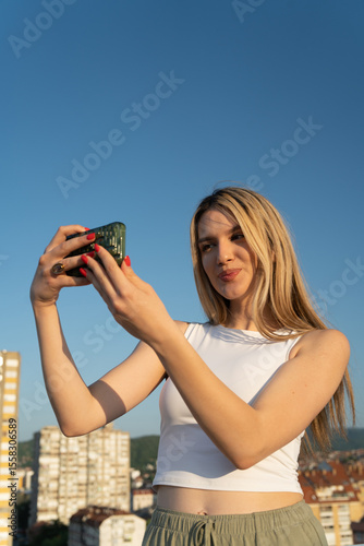 Young woman taking a selfie with a phone against the blue sky