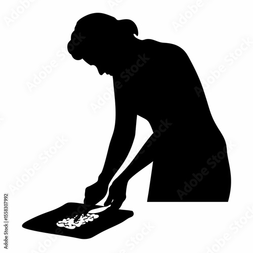 Silhouette of a woman cutting food on a cutting board with a knife in a kitchen preparation scene