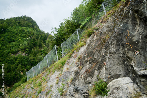 A sturdy fence lines a steep rocky slope, designed to protect the area from potential rockfall hazards.