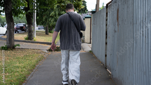 Man walking alone on a sidewalk in an urban area, surrounded by trees and parked cars