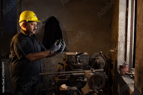 Photography Engineer in protective workwear inspecting lathe at factory