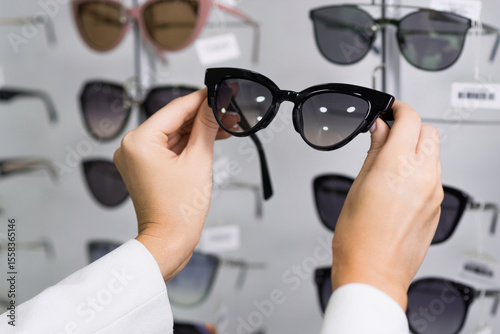 Close-up of hands of a young woman who chooses sunglasses on the showcase for purchase in an optical store. Optometry, eyesight, eyeglasses, accessories, fashion, lifestyle