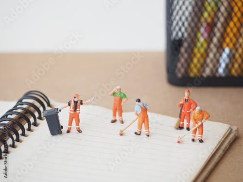 Mini toy pf action figure at table with blurred background. Miniature photography concept design. Diorama of cleaning crew at office desk with stationary stuff.