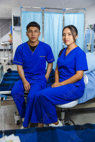 Two nurses in blue scrubs sitting in a hospital room after work, socializing and relaxing.