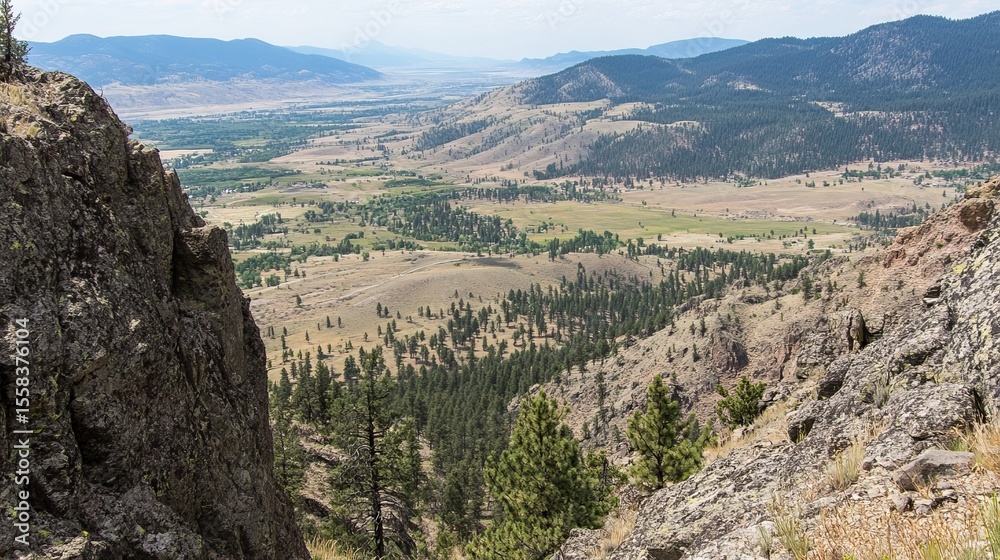 Fototapeta premium Panoramic view of a valley nestled between rocky mountains, showcasing diverse terrain, vegetation, and distant mountain ranges under a clear sky