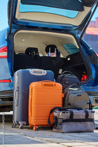 Suitcases and bags in front of open car trunk, standing on pavement near suburban house. Luggage ready for loading in vehicle before travel or moving. Concept of relocation or road trip