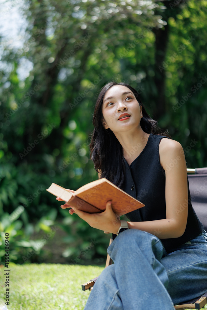 Obraz premium Young woman reading a book and daydreaming outdoors