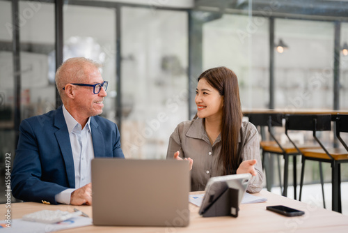 Businesspeople discussing and working using laptop and tablet in modern office, senior businessman and young businesswoman talking and working together