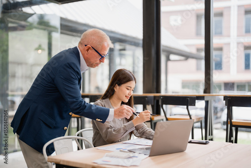Senior manager coaching young asian businesswoman and explaining new project using laptop and analyzing financial charts together at the office