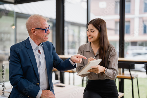Senior manager explaining company strategy while young businesswoman takes notes during an informal meeting in a modern office space, fostering collaboration and communication