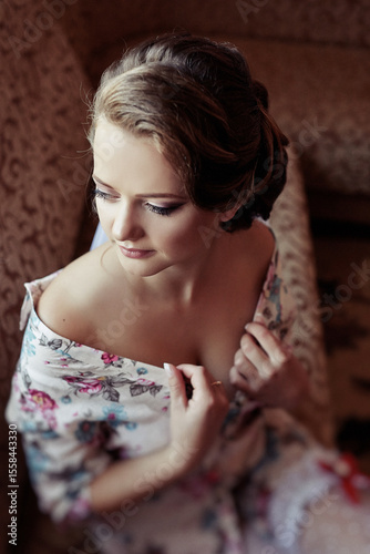 A woman in a floral dress is sitting on a couch. She is wearing a necklace and has her hand on her chest