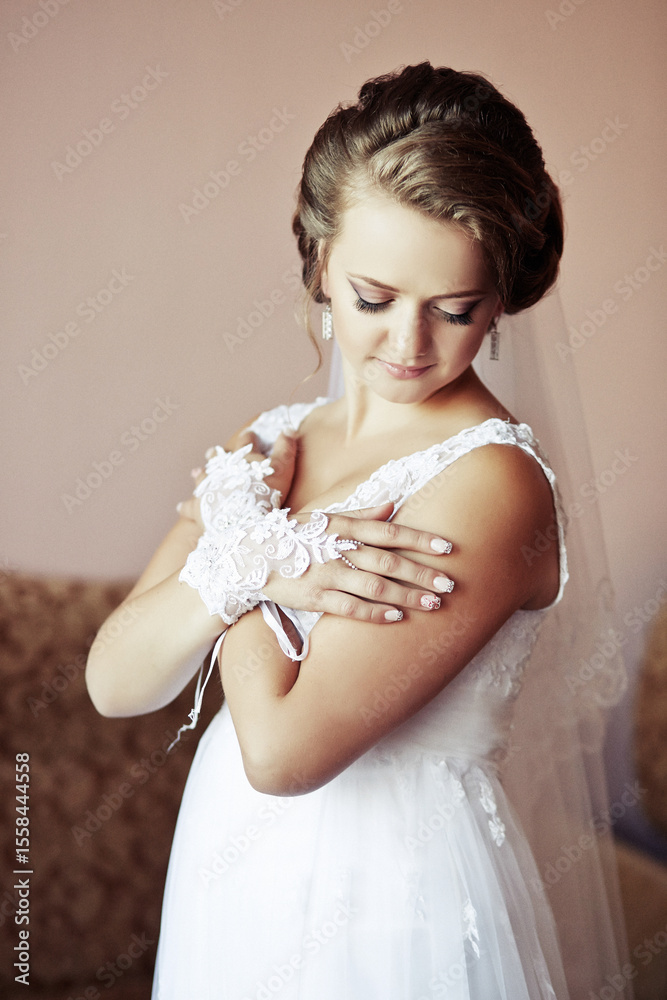 A woman in a white dress is wearing a lace glove and a veil. She is standing in front of a couch A woman in a white dress is wearing a lace glove and a veil. She is standing in front of a couch