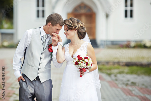 A bride and groom are standing in front of a church, with the bride holding a bouquet