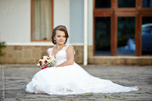 A young woman in a white dress sits on the ground with a bouquet of flowers in her lap
