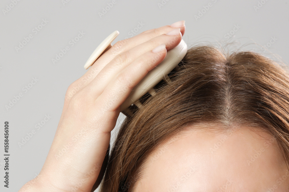 Fototapeta premium Girl doing herself a head massage using a scalp massager, stimulating hair growth, microcirculation, help to distribute natural oils more evenly across the scalp