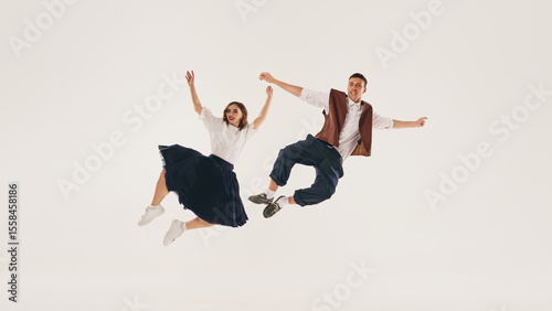 Retro lindy hop dancers perform a mid-air jump against a plain white background. Concept of vintage dance styles and joyful expression.