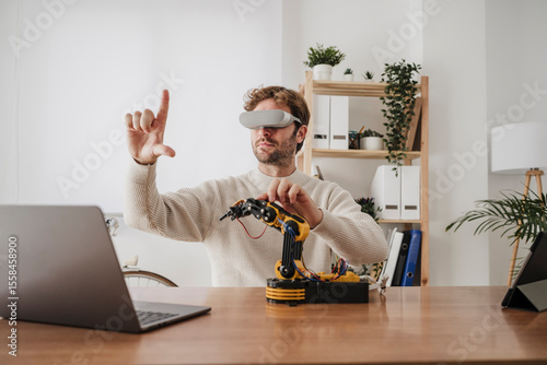 Engineer with VR Goggles gesturing by robotic arm at office