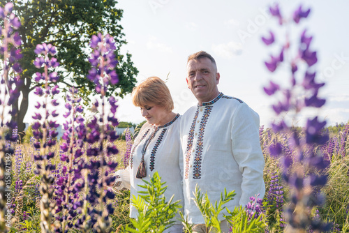 Happy senior Ukrainian couple in traditional embroidered shirts standing in a blooming field, celebrating love and family togetherness. romantic family lifestyle. unity and national pride concept. 
