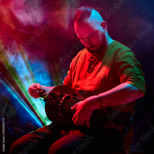 A musician skillfully plays the hurdy-gurdy beneath vibrant red and blue stage lights. Concept of unique music performances and atmospheric stage lighting effects.