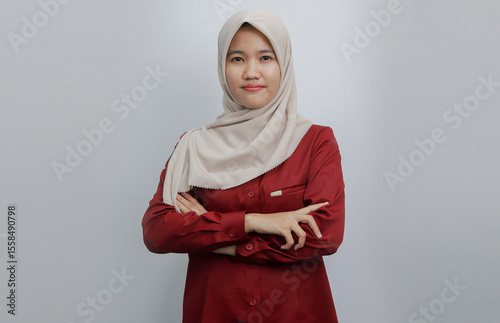 Foto A confident Muslim woman wearing a beige hijab and red shirt poses with her arms crossed against a plain background