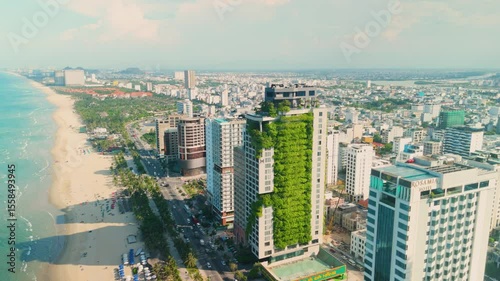 Aerial view capturing da nangs cityscape with a prominent green building draped in vegetation, highlighting sustainable architecture among modern hotels and the stunning coastline