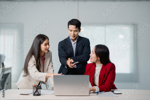 Three asian businesspeople are discussing work, using a laptop in a modern office, collaborating on a project and sharing ideas in a dynamic and productive environment