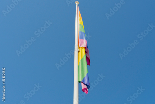 Rainbow flag on a flagpole in the wind against a blue sky photo