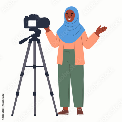 A woman in a hijab stands beside a camera on a tripod gesturing with her hands