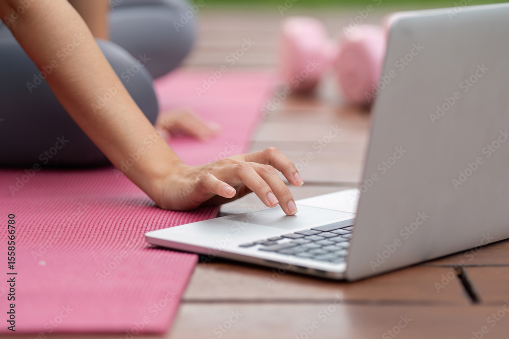 Fototapeta premium Remote Work and Fitness. Woman using laptop for online workout while seated on exercise mat.