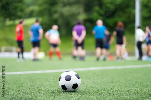 Soccer ball on green field with unrecognizable people photo