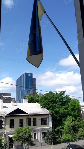 Ukrainian flag waving against blue sky. Cityscape view