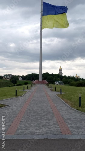 Ukraine flag waves on flagpole. Gray stone road on foreground