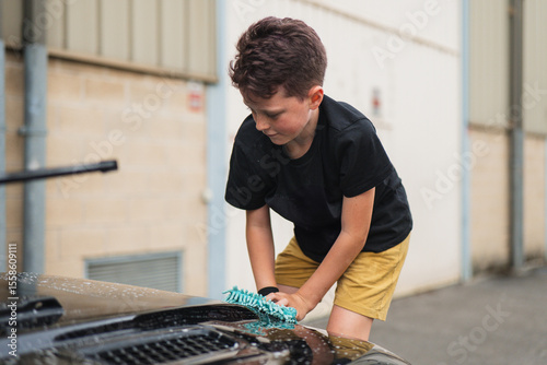 Child cleaning car hood with a sponge