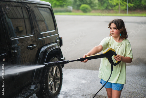 Young girl using a pressure washer on vehicle exterior